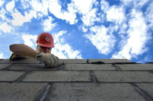 Construction worker building brick wall skyward.