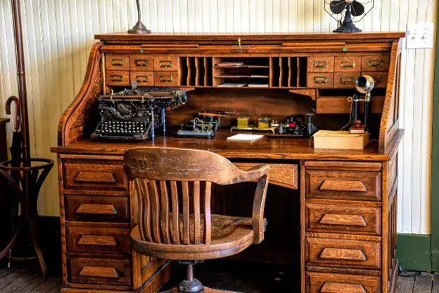 Vintage wooden roll-top desk with a classic chair and typewriter.