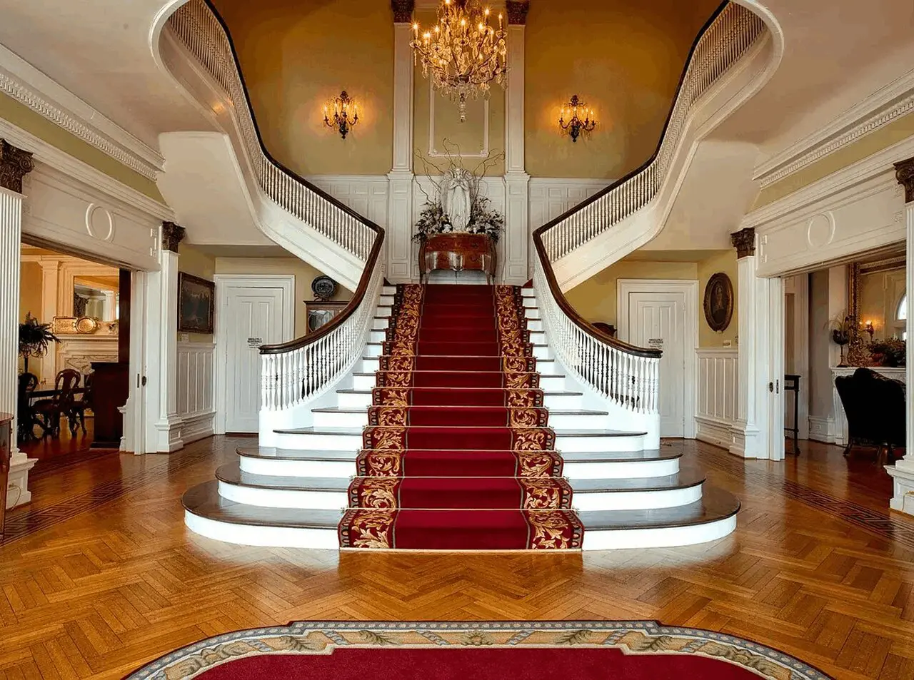 Red-carpeted dual staircase with ornate chandelier